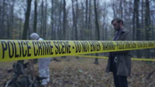 Police crime scene tape in a forest with investigators