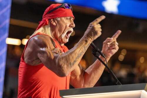 A muscular man in a red bandana passionately speaking at a podium