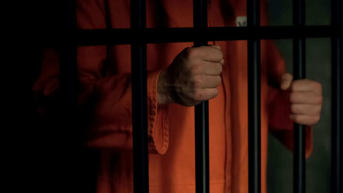 Person in orange prison jumpsuit behind bars