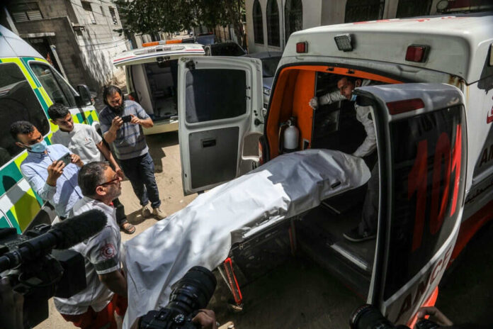 People loading stretcher into ambulance surrounded by onlookers