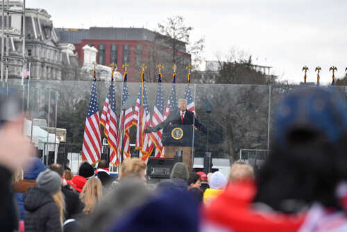 A speaker at a podium with American flags in the background addressing a crowd