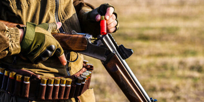 Person loading shotgun with red shell outdoors