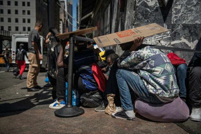 People sitting under cardboard on a city sidewalk