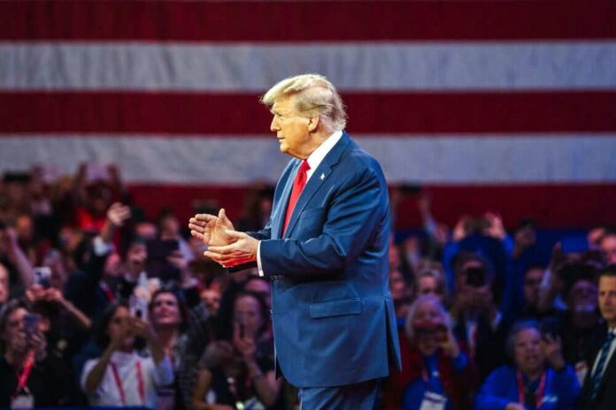 Man in blue suit gesturing with American flag background