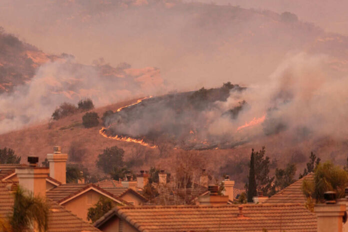 Wildfire approaching residential area with smoke rising