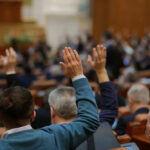 People raising hands in a crowded meeting room