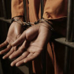 Person handcuffed behind prison bars in orange jumpsuit