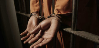 Person handcuffed behind prison bars in orange jumpsuit