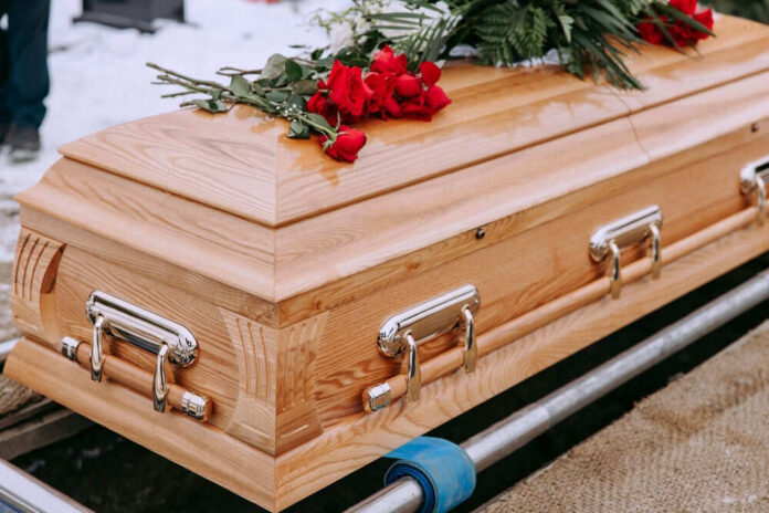 Wooden coffin with red roses and green leaves