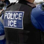 ICE CRUSHES California Sanctuary — 118 ARRESTED! Close-up of a police officers uniform with POLICE ICE on the back